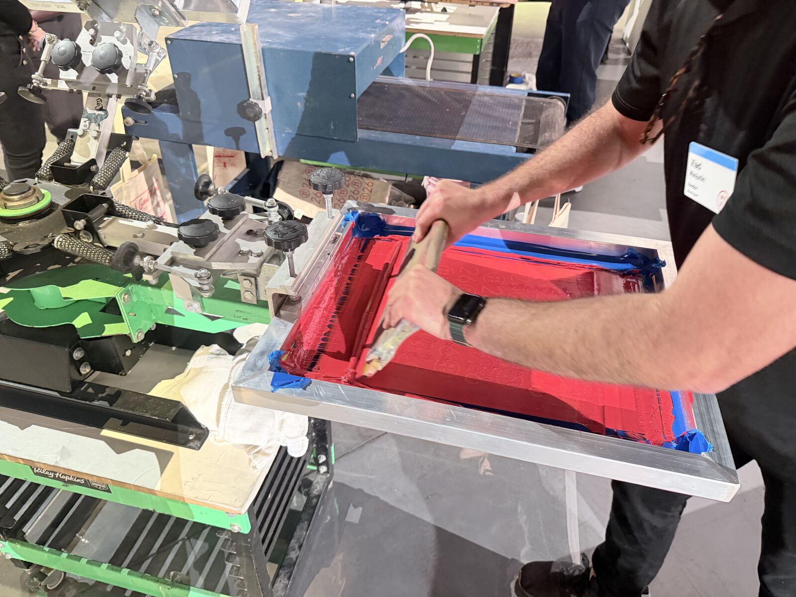 Close-up of screen printing equipment showing red and blue squeegees and a printing frame in operation