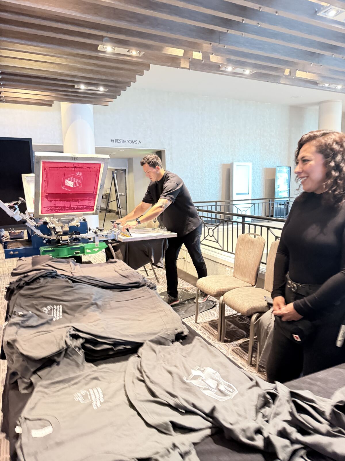 Live screen printing demonstration with an operator at work and decorated t-shirts displayed on wall shelving