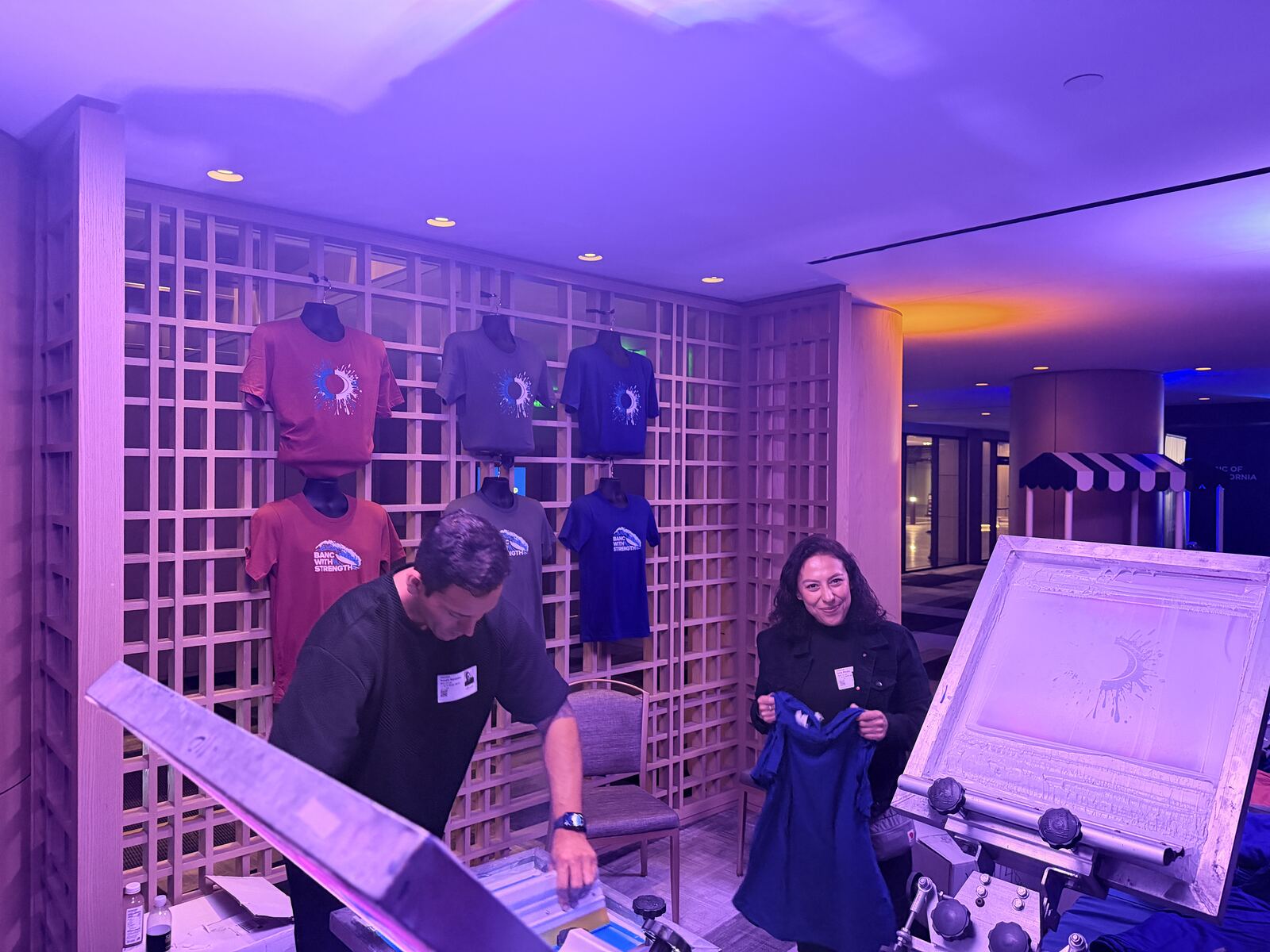Professional display of decorated apparel and branded merchandise under dramatic purple lighting at an event booth